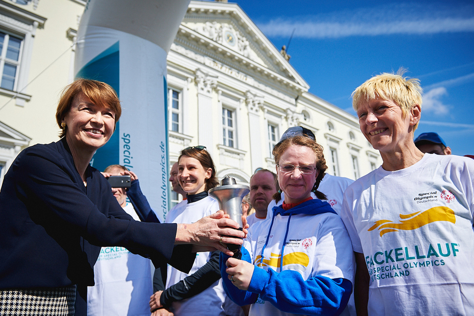 Elke Büdenbender übergibt die Fackel an die erste Läufergruppe vor dem Schlossportal zum Auftakt des Special Olympics Fackellaufs