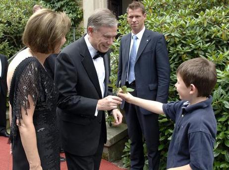 Bundespräsident Horst Köhler wird von einem kleinen Jungen mit einer Rose begrüßt (daneben: Eva Luise Köhler).