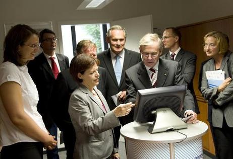 Bundespräsident Horst Köhler im Gespräch mit einer Mitarbeiterin an einem Computer beim Rundgang durch die Nationale Deutsche Anti Doping Agentur (dahinter: Armin Baumert, Vorstandsvorsitzender der NADA).