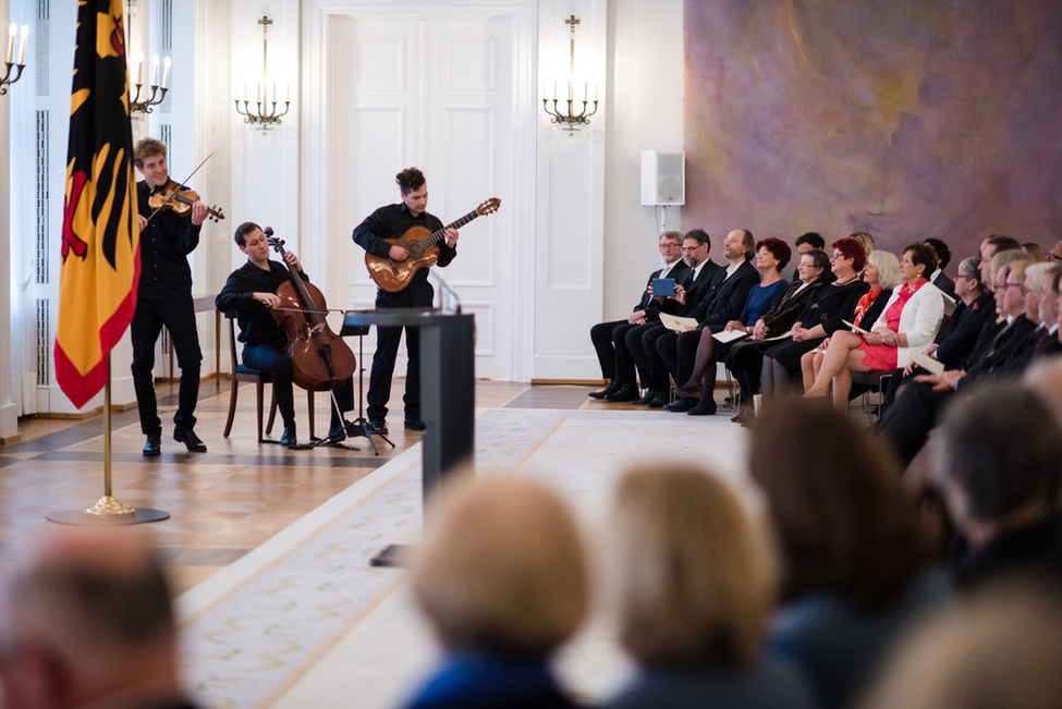 Bundespräsident Frank-Walter Steinmeier lauscht der musikalischen Untermalung des Ensembles 'Wild Strings'  bei der Verleihung des Verdienstordens zum Tag des Ehrenamtes im Großen Saal von Schloss Bellevue