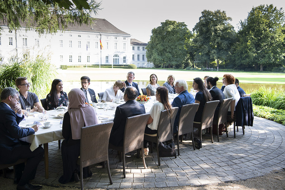 Bundespräsident Frank-Walter Steinmeier und Elke Büdenbender tauschen sich während eines Gesprächs mit Bürgerinnen und Bürgern aus der Nachbarschaft bei einer türkisch-deutschen Kaffeetafel im Schlosspark aus