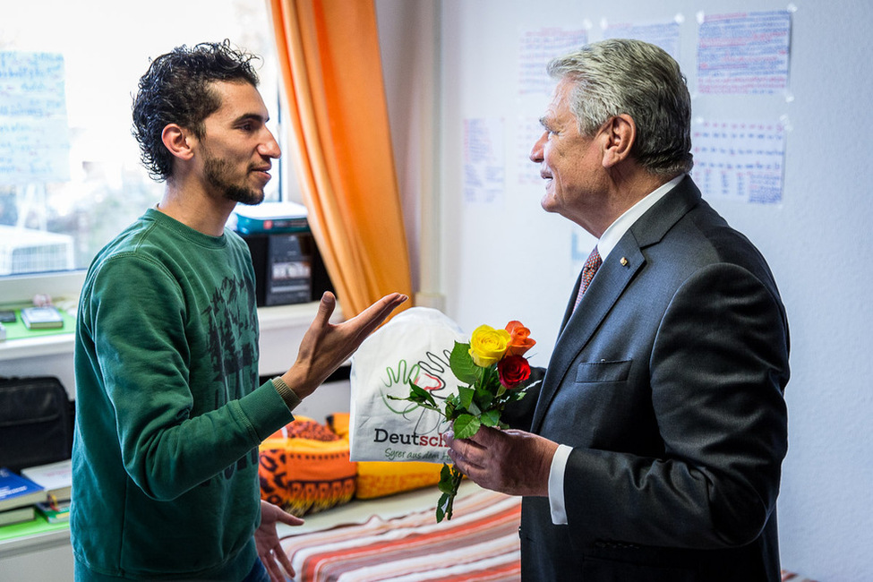 Bundespräsident Joachim Gauck erhält während seines Besuchs in der Flüchtlingsunterkunft am ehemaligen Bastei-Lübbe Verlagsgebäude in Bergisch Gladbach von Abd Aljasem, einem Flüchtling aus Syrien, Blumen und ein selbstgestaltetes T-Shirt 