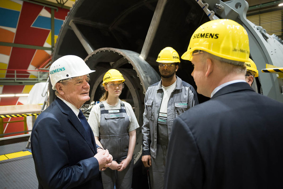 Bundespräsident Joachim Gauck im Austausch mit Jan-Marc Lischka, Sprecher der Betriebsleitung, und zwei Auszubildenden während des Rundgangs im Gasturbinenwerk von Siemens in Berlin