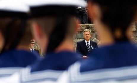 Bundespräsident Christian Wulff spricht an einem Mikrofon. Im Vordergrund sind drei junge Männer in weiß-blauer Matrosenuniform zu erkennen. 