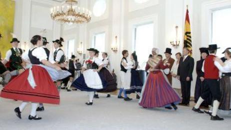 Tanzpaare in bunten Trachten im Großen Saal des Schlosses; Bundespräsident Horst Köhler und Eva Luise Köhler schauen zu.