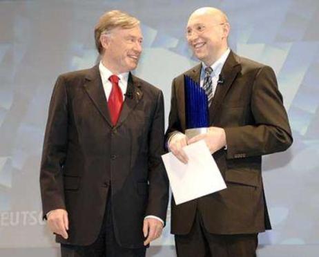 Bundespräsident Horst Köhler und der Preisträger - in der Hand die blaue Preisskulptur - stehen auf der Bühne vor einer blauen Wand. 