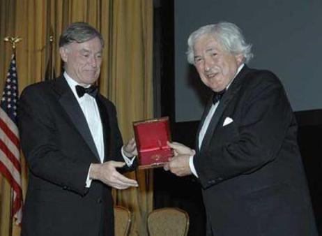 Bundespräsident Horst Köhler steht neben James D. Wolfensohn; dieser hält ein aufgeklapptes Kästchen mit rotem Futter und einer Münze darin in der Hand; dahinter die amerikanische Flagge