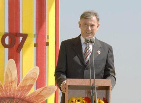 Bundespräsident Horst Köhler steht hinter einem Rednerpult im Freien; links hinter ihm eine gelb-rot gestreifte Wand, rechts der blaue Himmel 