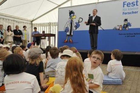 Der Bundespräsident steht auf der Bühne an einem Mikofon, im Hintergrund eine blaue Wand mit der Comicfigur "Elli", vor der Bühne sitzen Kinder auf Kissen