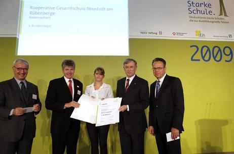 Bundespräsident Horst Köhler steht zusammen mit einer jungen Frau, die eine Urkunde hält, und drei Herren vor einer gelben Rückwand mit der Aufschrift "Starke Schule 2009"