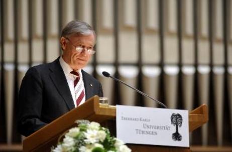 Bundespräsident Horst Köhler steht an einem Rednerpult. Weiße Blumen und das Logo der Universität Tübingen sind im Vordergrund zu sehen. 