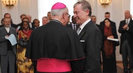 Der Bundespräsident reicht dem katholischen Nuntius die Hand. Im Hintergrund sind Diplomaten anderer Länder zu sehen. 