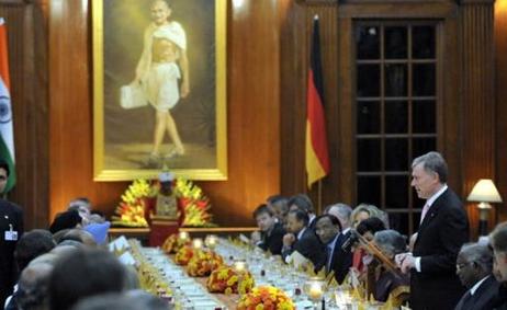 Bundespräsident Horst Köhler steht an einem kleinen Rednerpult an einer langen, festlich gedeckten Tafel, an der viele Menschen sitzen. Im Hintergrund sind ein Bild Gandhis mit goldenem Rahmen zu sehen sowie die Flaggen Indiens und Deutschlands. 