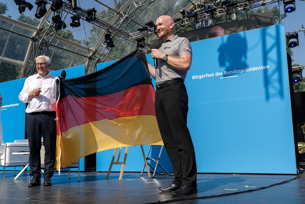 Bundespräsident Frank-Walter Steinmeier und Alexander Gerst halten eine Deutschlandflagge hoch, die Alexander Gerst mit ins All auf die Raumstation ISS genommen hatte