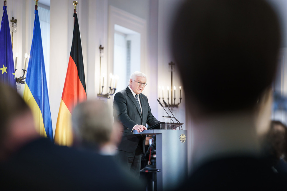 Bundespräsident Steinmeier steht an einem Rednerpult vor einer europäischen, einer ukrainischen und einer deutschen Flagge.