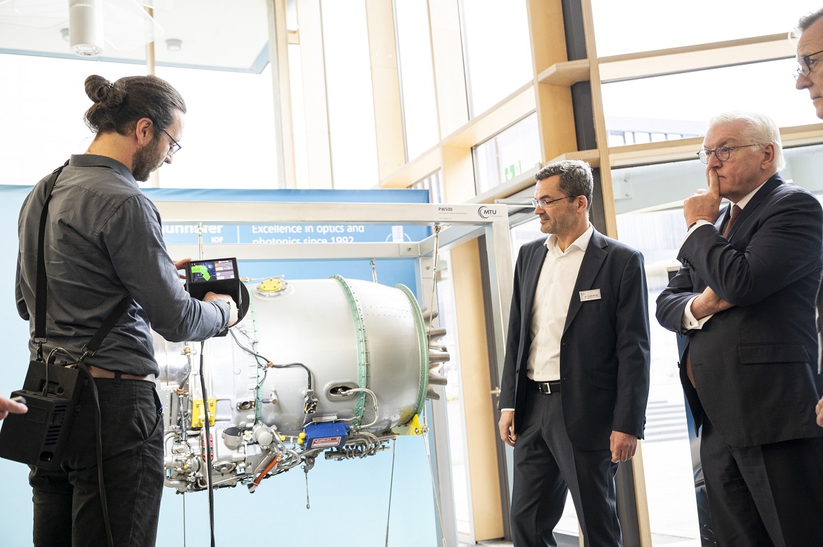Bundespräsident Frank-Walter Steinmeier lässt sich von einem Forscher den 3D-Handscanner zeigen, der eine Flugzeugturbine scannt (© Bundesregierung/Guido Bergmann) Bundespräsident Frank-Walter Steinmeier lässt sich von einem Forscher den 3D-Handscanner zeigen, der eine Flugzeugturbine scannt