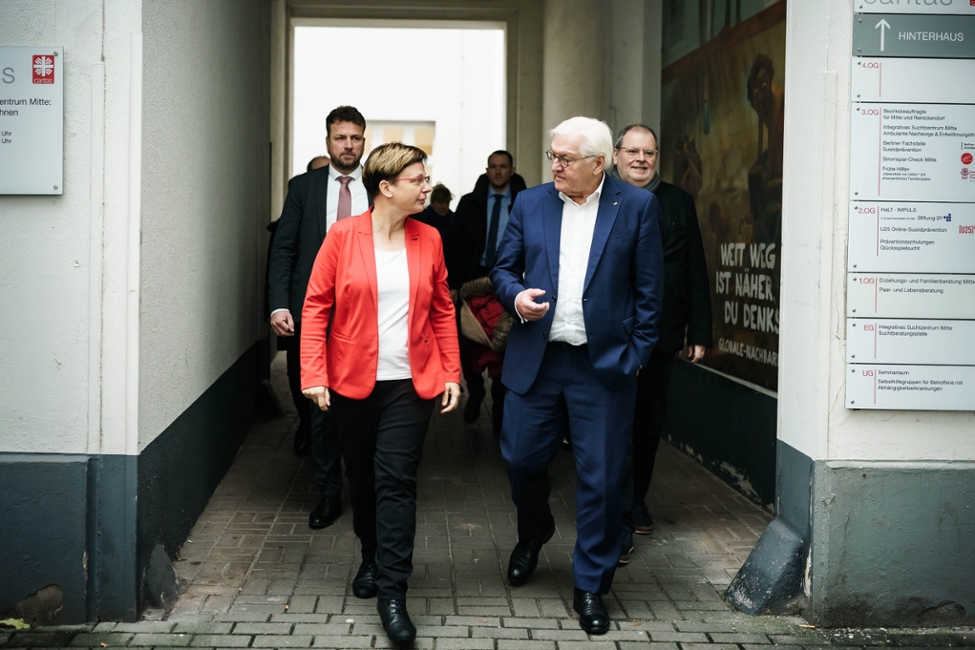 Bundespräsident Steinmeier läuft gemeinsam mit Ulrike Kostka durch den Innenhof am Haus der Caritas (© Bundesregierung/Jesco Denzel) Bundespräsident Steinmeier läuft gemeinsam mit Ulrike Kostka durch den Innenhof am Haus der Caritas